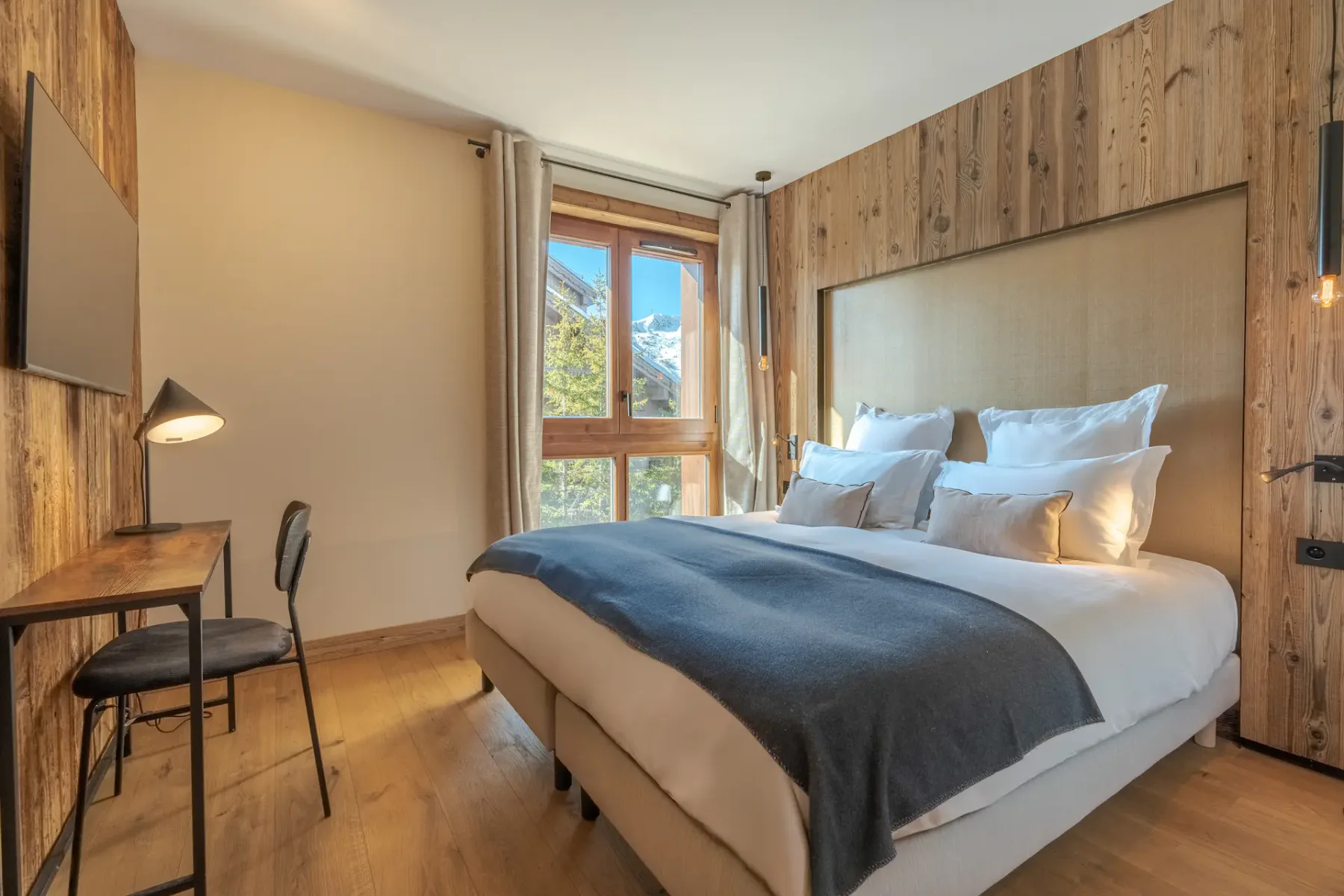 Un dormitorio con una cama, un escritorio pequeño y una ventana con vistas a los árboles.