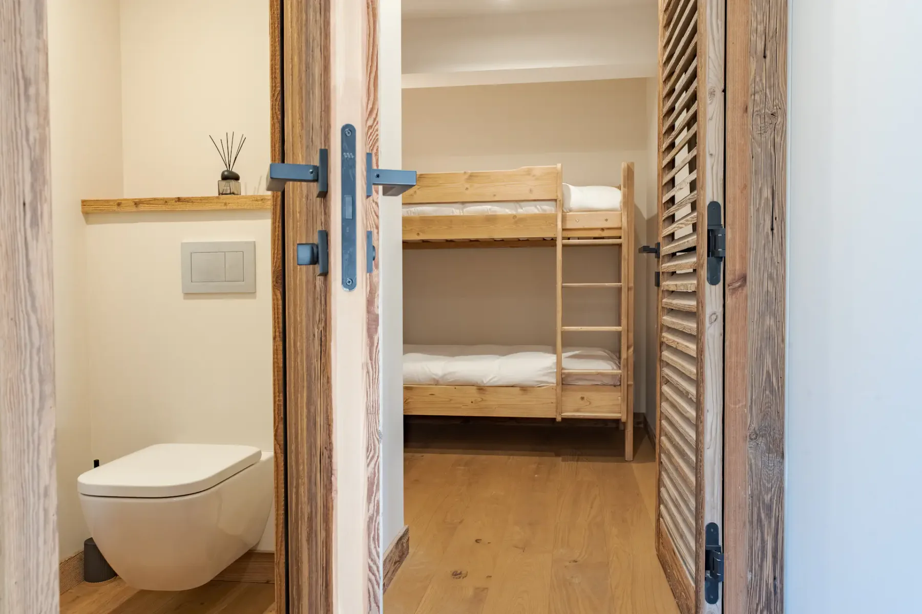 Vista de una pequeña habitación con literas y un inodoro, separados por puertas de madera.