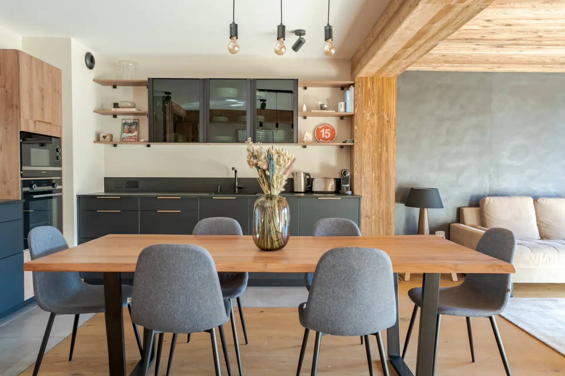 Una cocina y comedor con una mesa de madera y asientos grises.