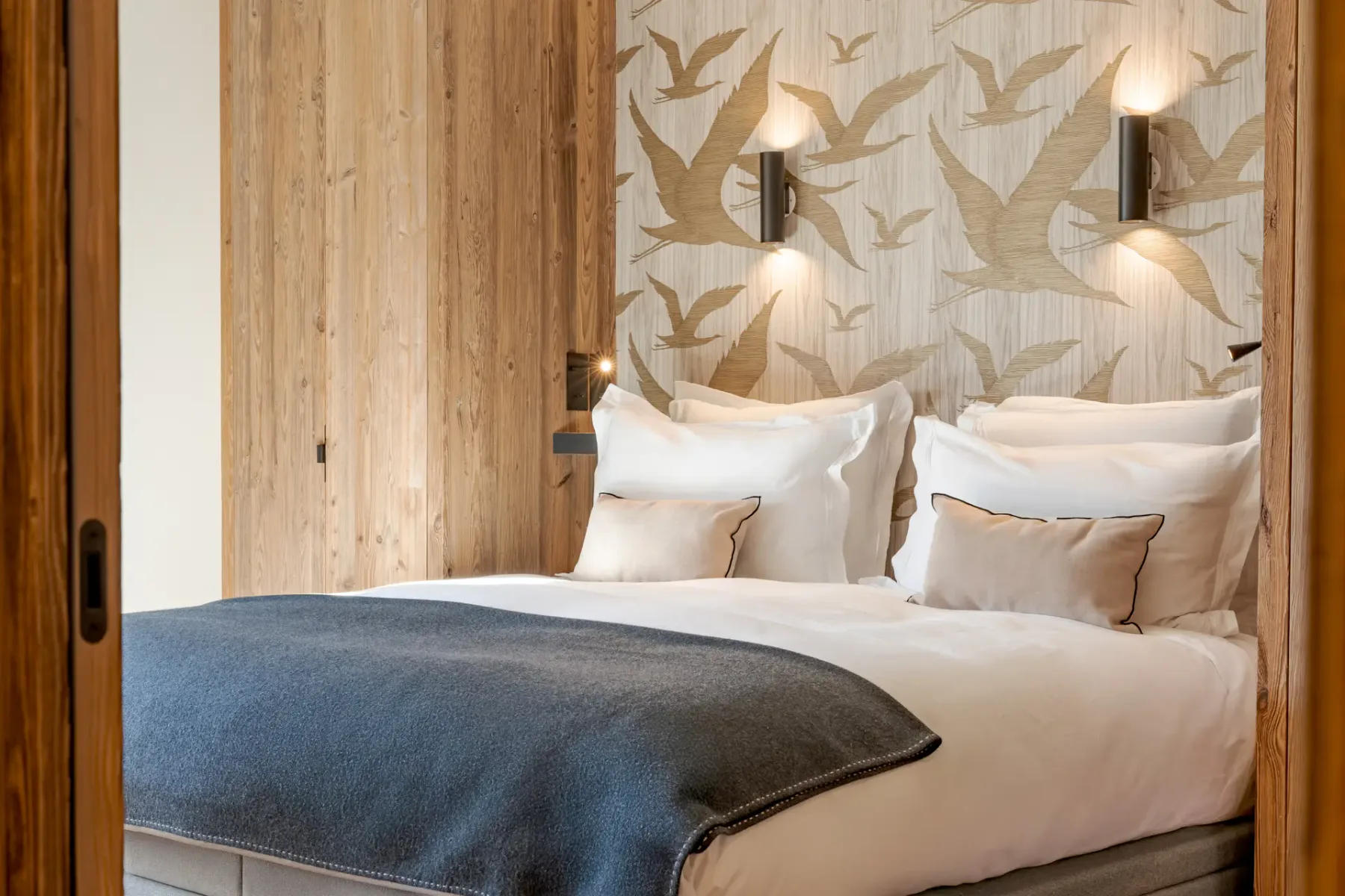 Un dormitorio con una cama, papel pintado con motivos de pájaros y paredes revestidas de madera.