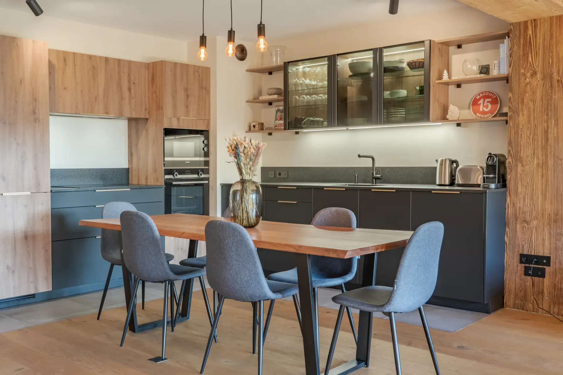 Cocina con una mesa de comedor de madera y asientos grises bajo lámparas colgantes.
