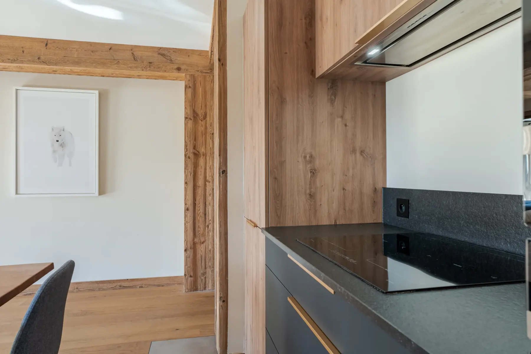 Cocina con muebles de madera y una encimera oscura junto a un comedor.