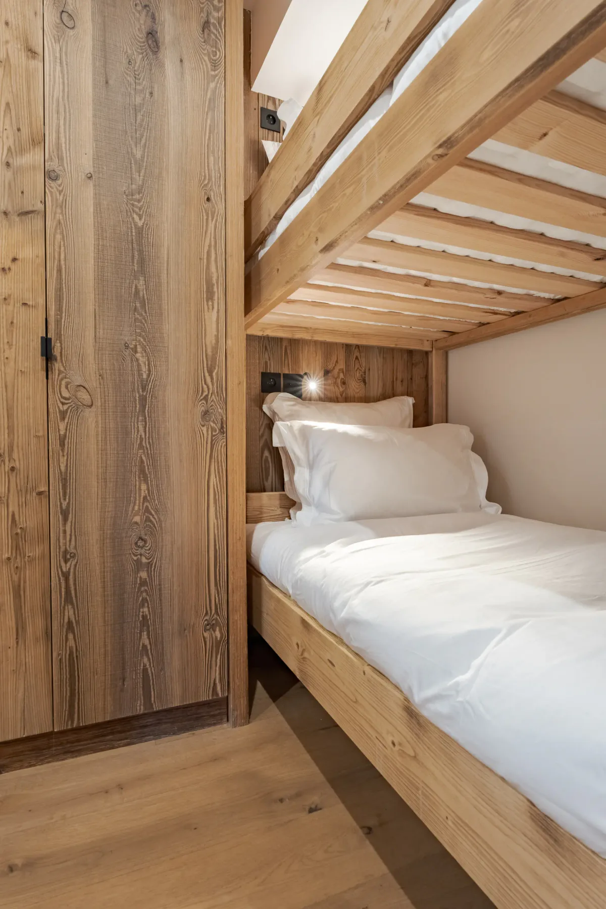 Una litera de madera con ropa de cama blanca está junto a un armario alto de madera.