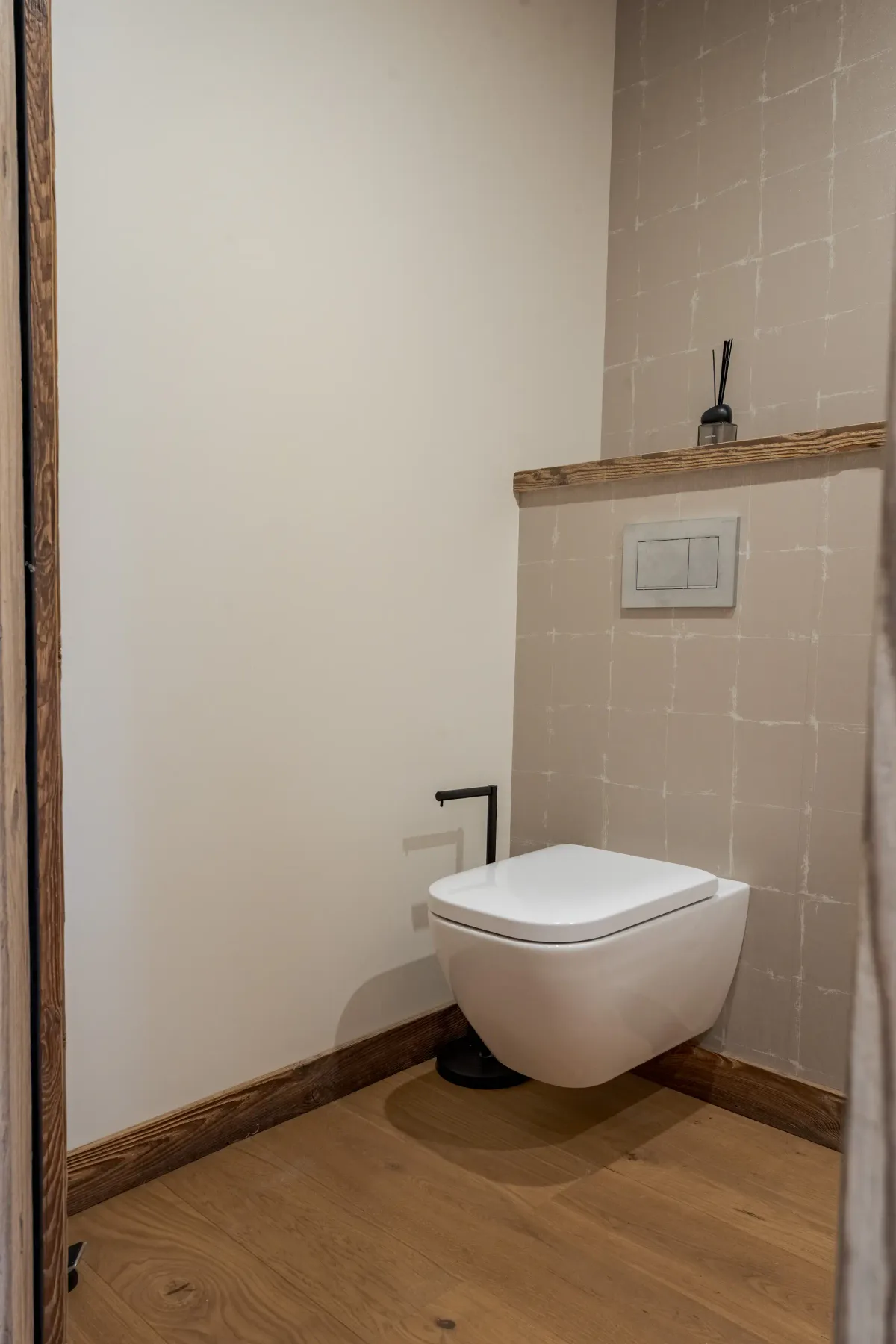Un baño minimalista con un inodoro suspendido y un pequeño estante encima.