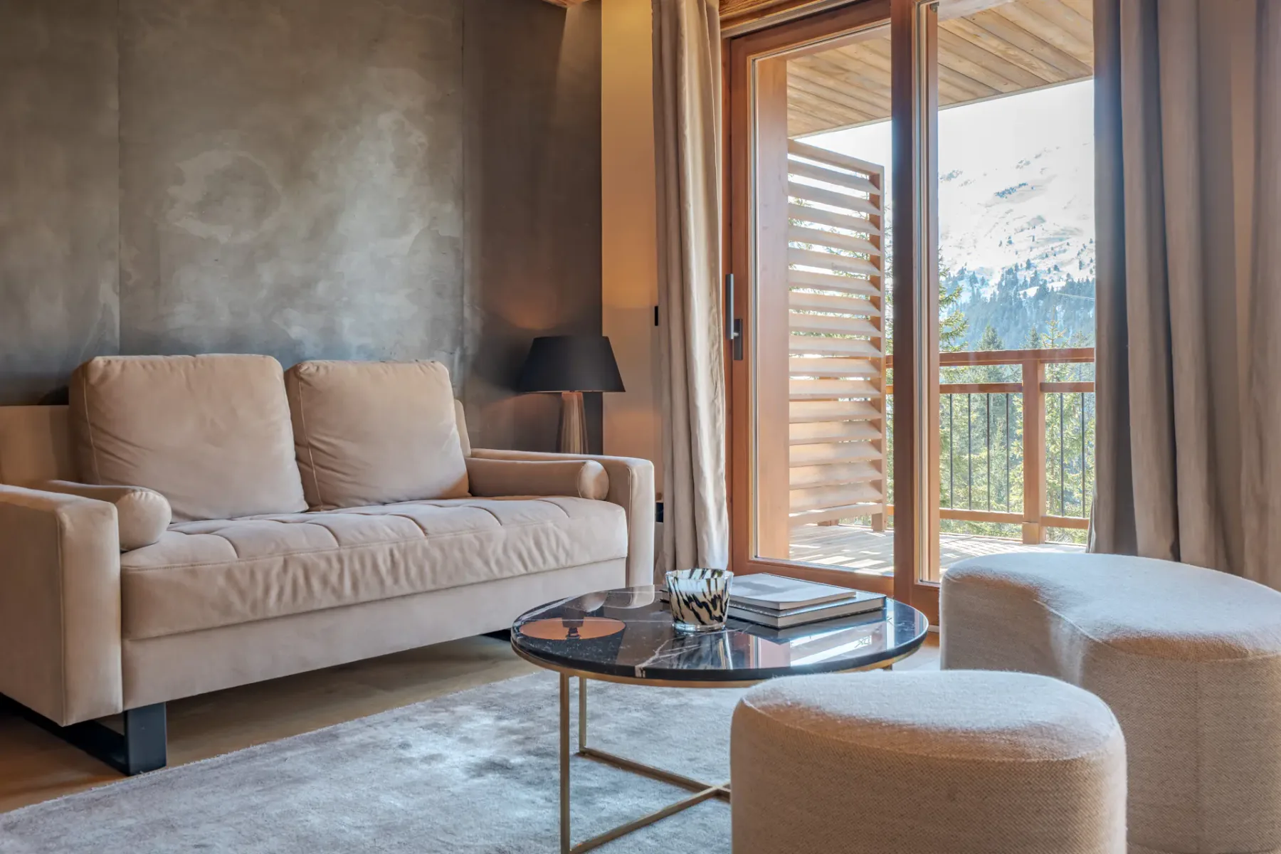 Una sala de estar con asientos beige, una mesa de centro redonda de cristal y vistas a montañas nevadas por la ventana.