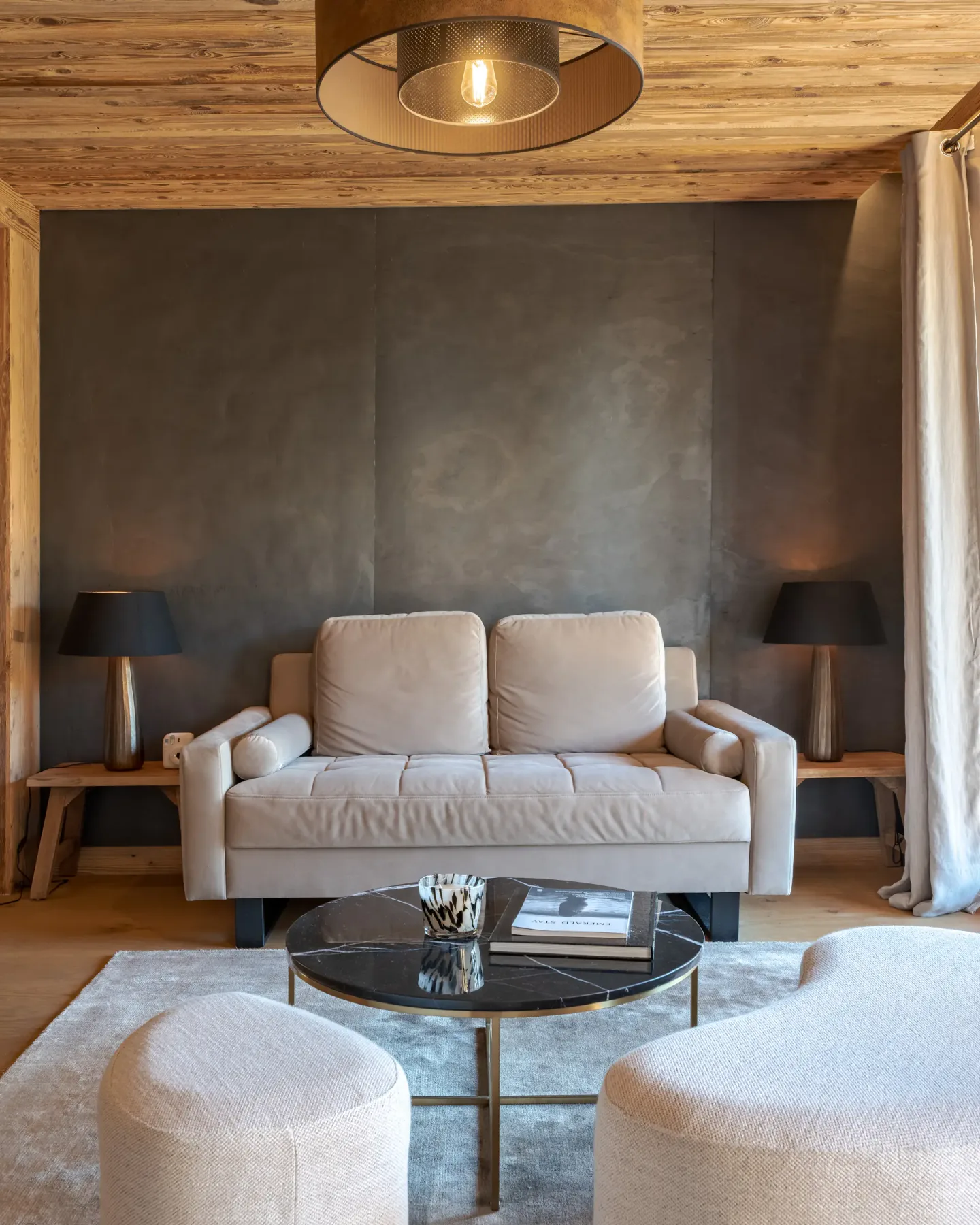 Una sala de estar con asientos, una mesa de centro de cristal y cortinas junto a una ventana grande.