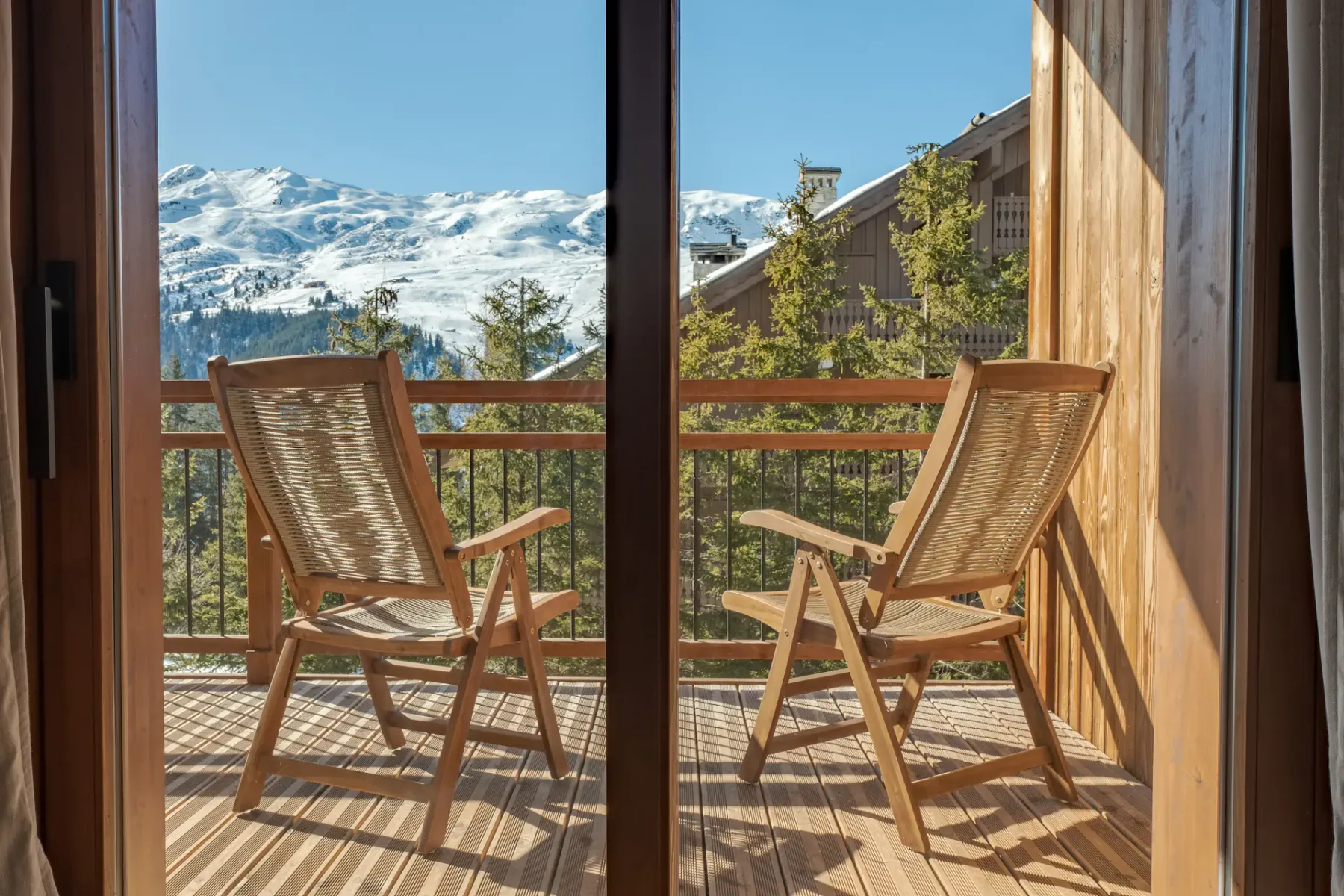 Dos sillas de madera están en un balcón con vistas a montañas nevadas.