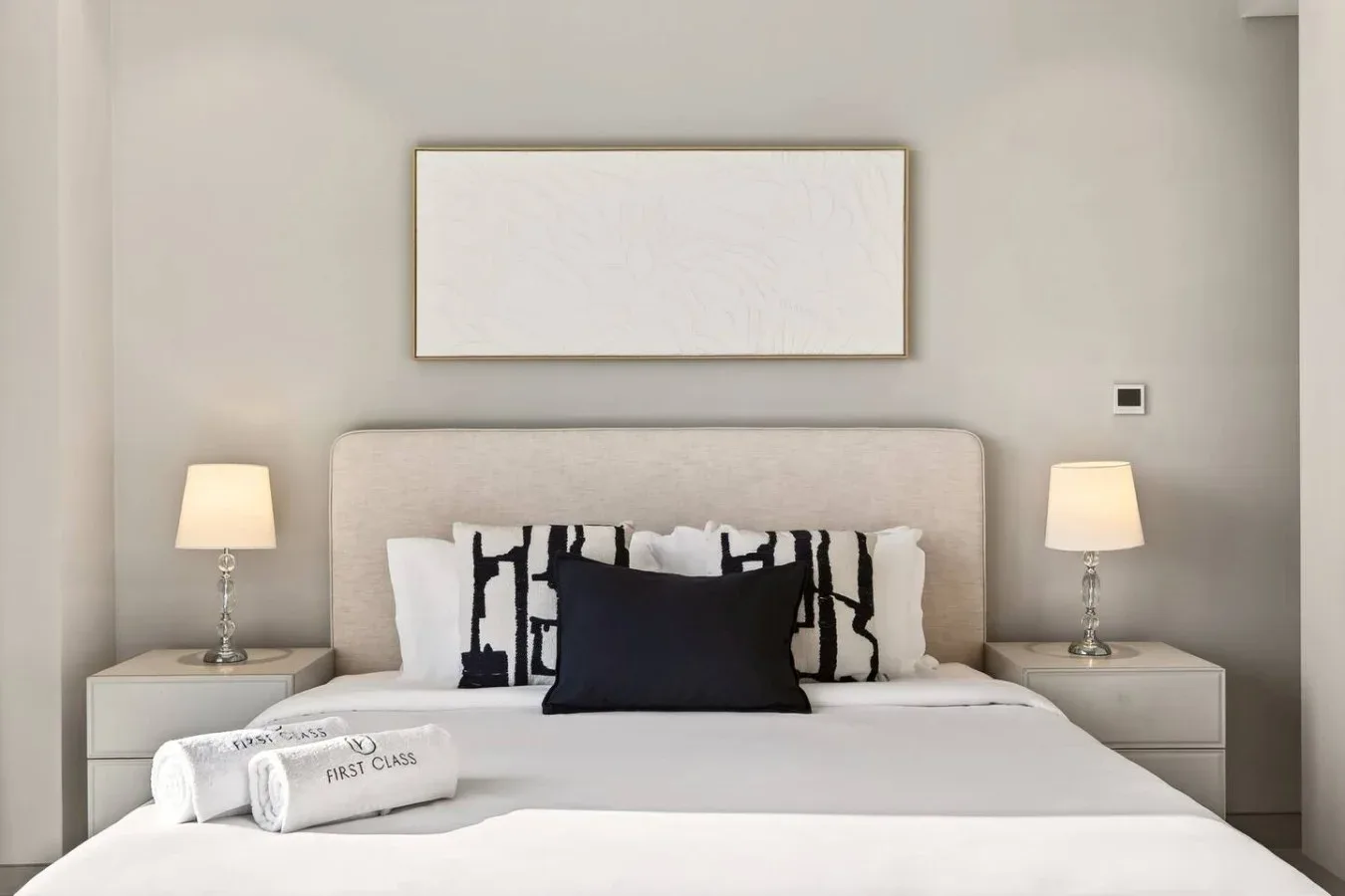 Una cama de dormitorio bien tendida, con almohadas y lámparas de noche a juego.