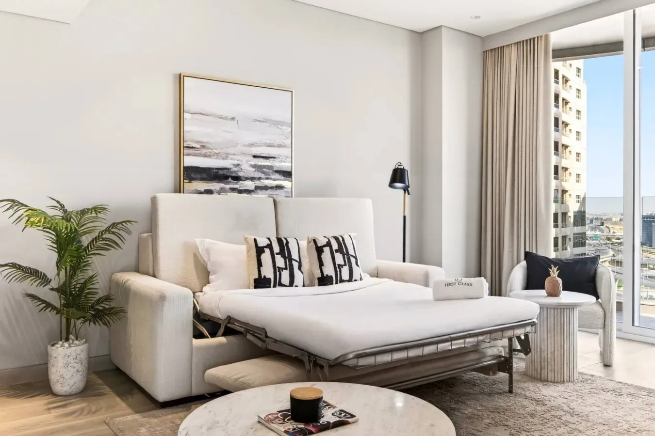 Una sala luminosa tiene un sofá cama blanco junto a una ventana grande.