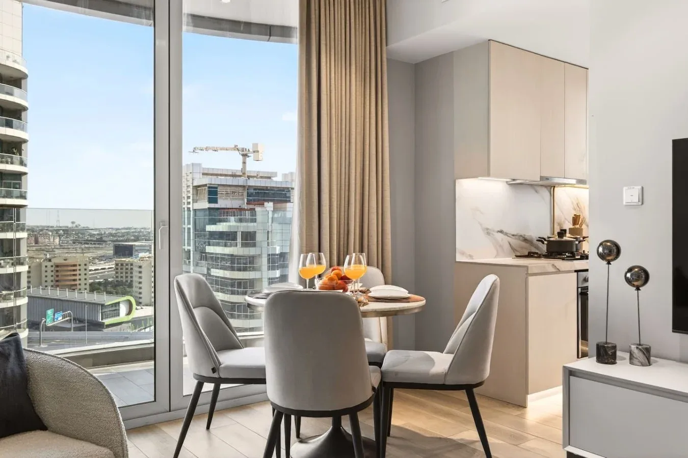 Un comedor luminoso con mesa y asientos junto a grandes ventanas con vistas a edificios de la ciudad.