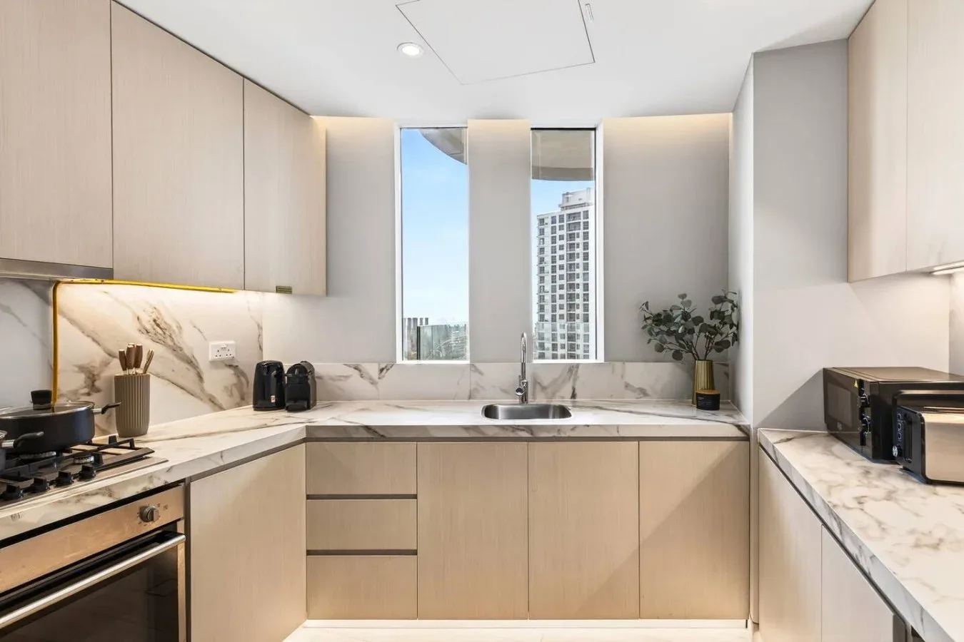 Una cocina moderna con gabinetes claros, encimeras veteadas y un fregadero bajo las ventanas.