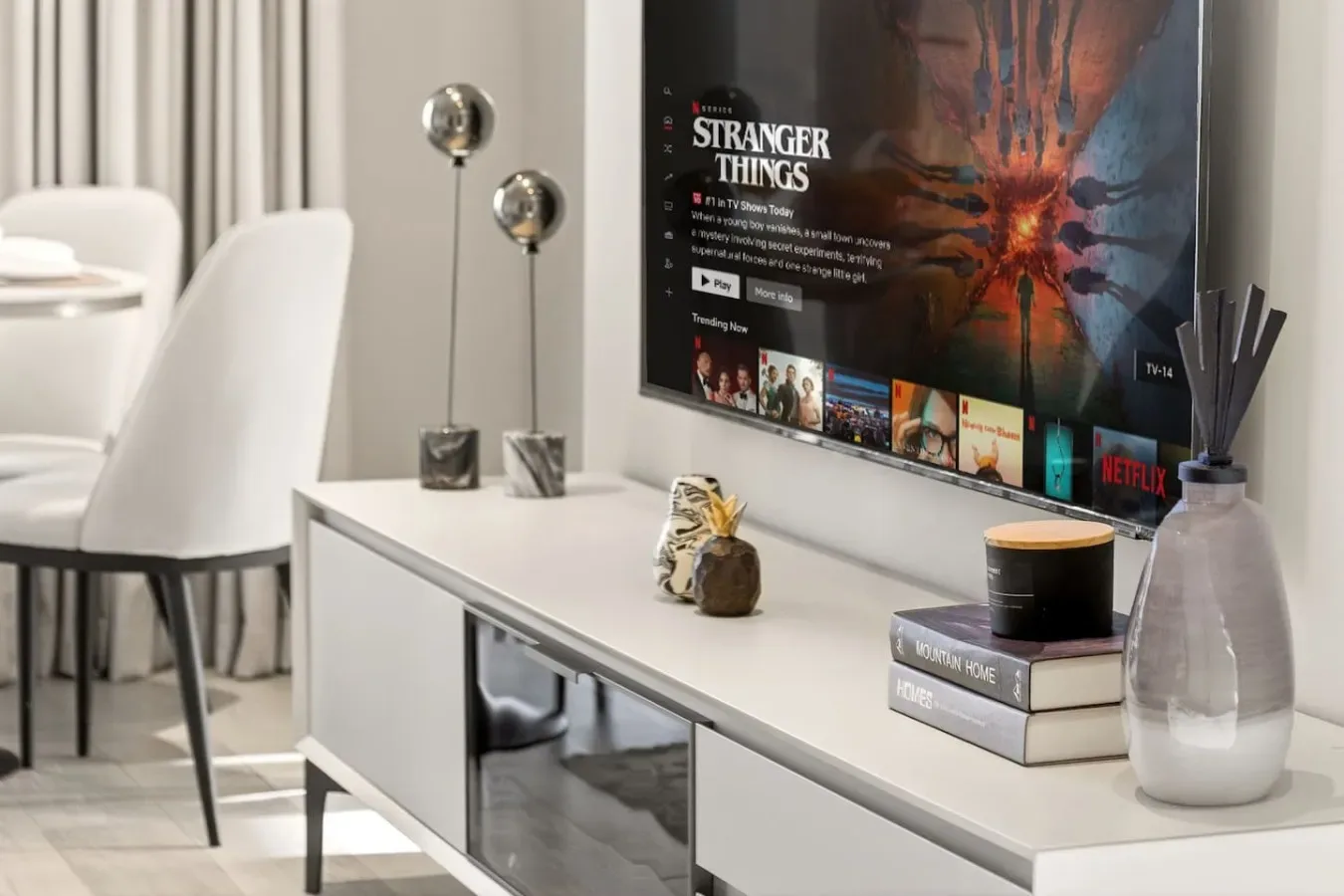 Una luminosa sala de estar y comedor tiene una consola larga bajo un televisor montado en la pared.