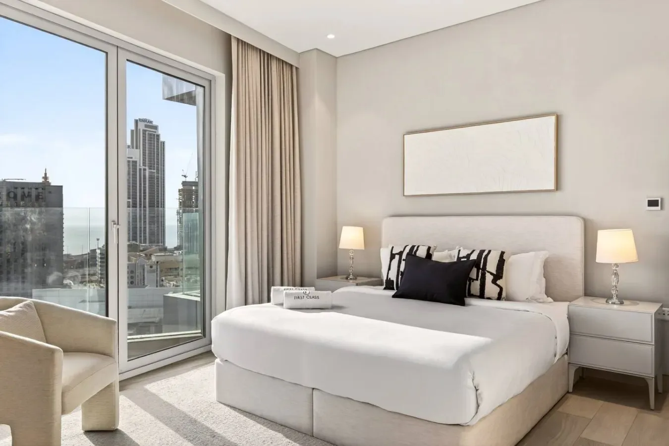 Un dormitorio luminoso con una cama bien tendida junto a grandes ventanas.