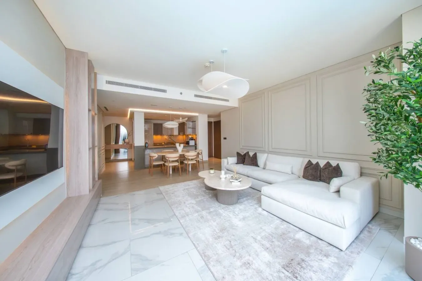 Una sala luminosa con asientos blancos, una mesa de centro y un comedor al fondo.
