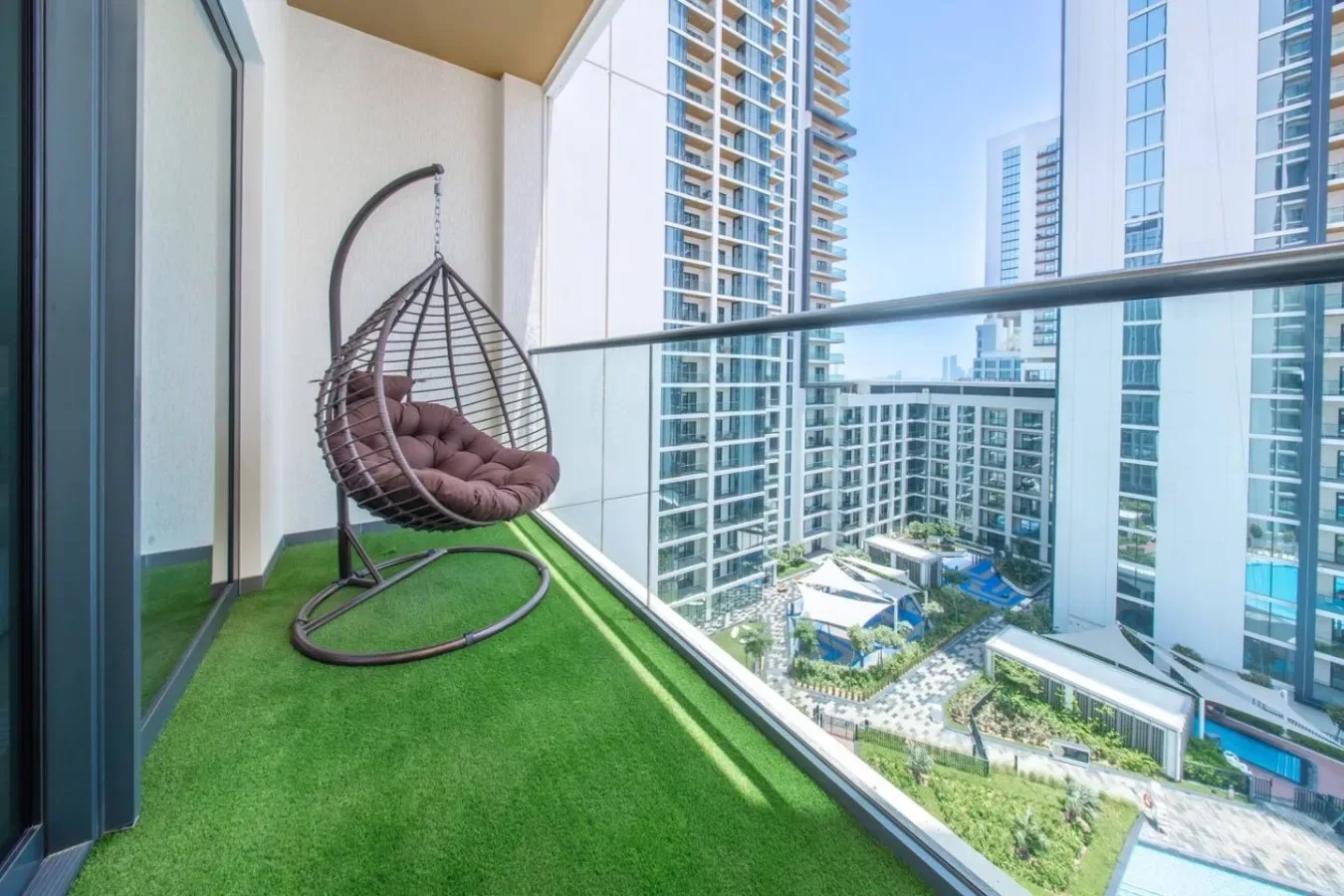 Un balcón con suelo verde y un asiento colgante da a edificios altos cercanos.