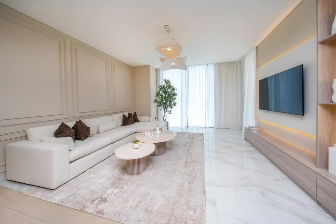 Una sala luminosa con asientos claros, una alfombra y un televisor en la pared.