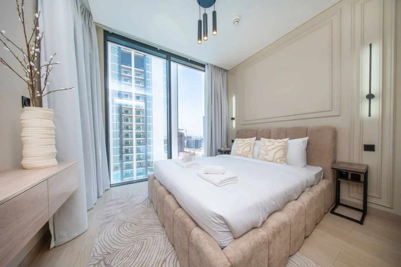 Un dormitorio con una cama bien tendida junto a grandes ventanas.