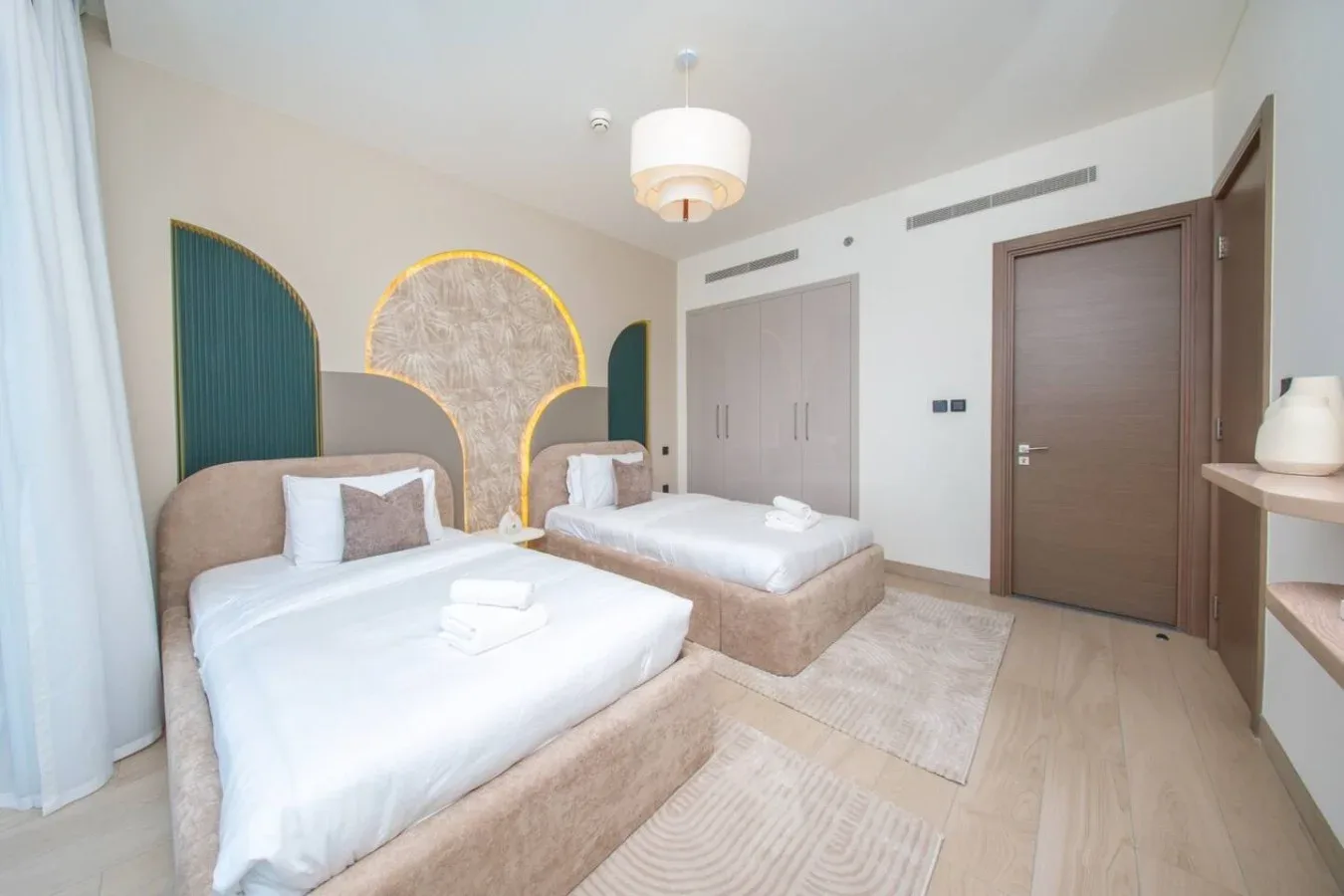 Un dormitorio con dos camas, ropa de cama clara y cabeceros decorativos curvos.