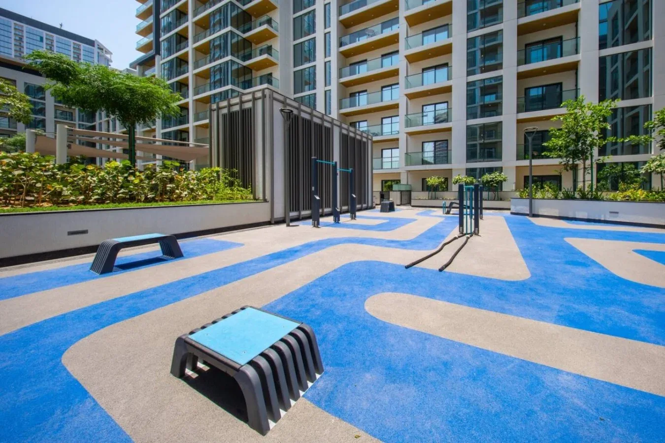 Una zona de ejercicio al aire libre con suelo azul y beige está entre edificios de apartamentos.