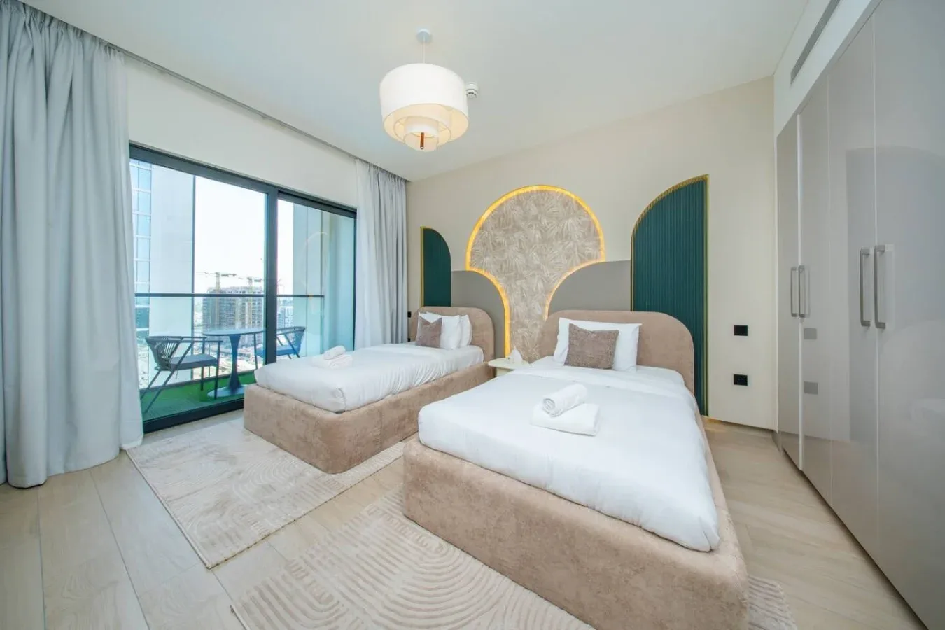 Un dormitorio luminoso con dos camas y puertas corredizas de vidrio que dan a un balcón.