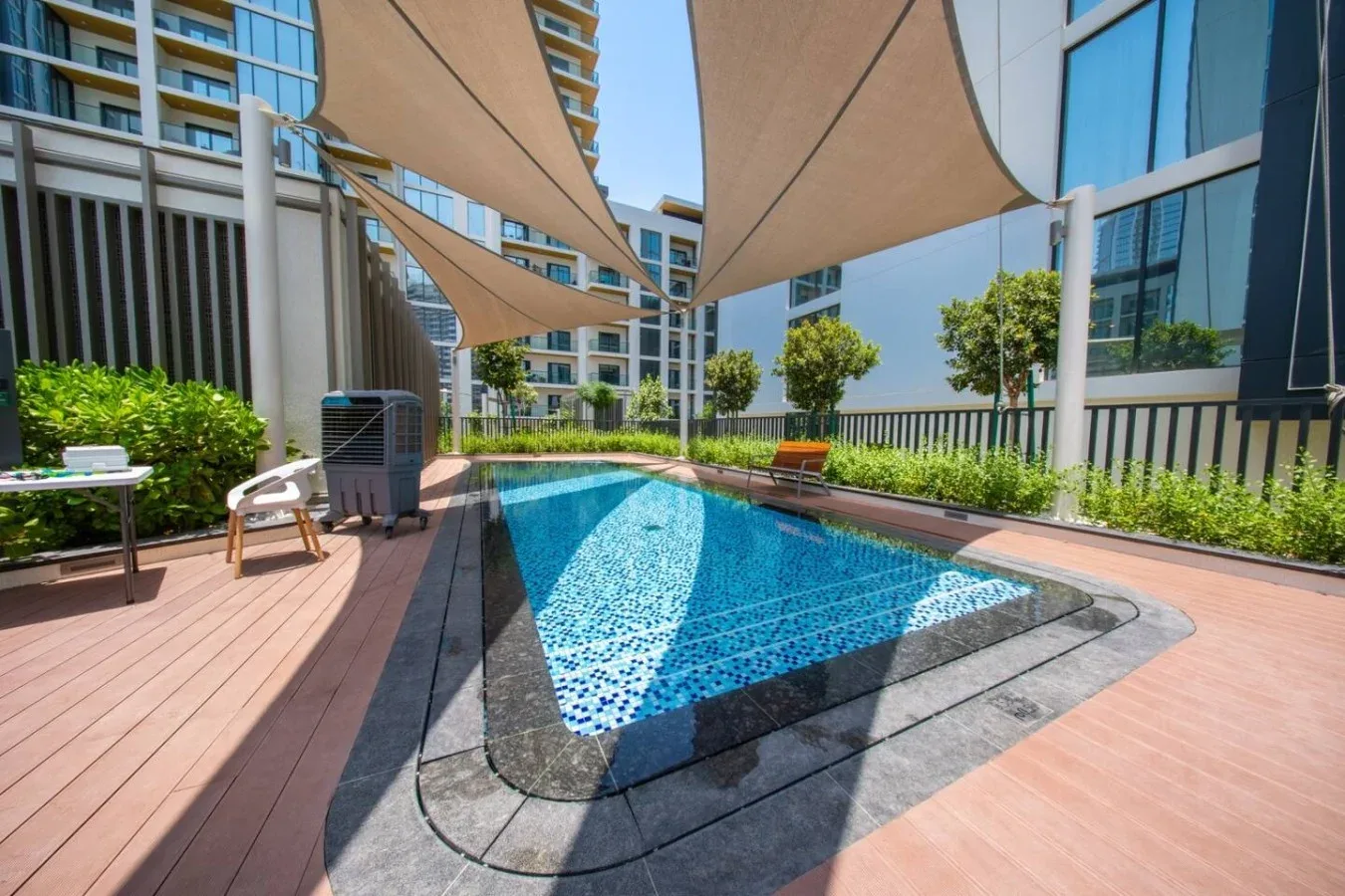 Una piscina al aire libre está junto a una terraza de madera bajo toldos.
