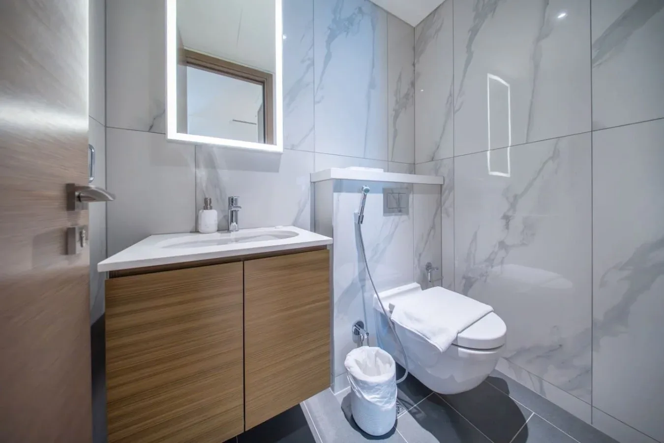 Un baño moderno con mueble de madera, inodoro suspendido y paredes de azulejos.