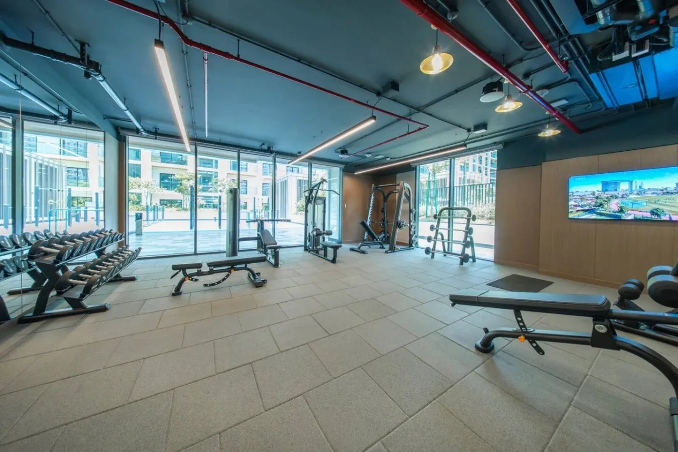 Un gimnasio con máquinas de ejercicio y bancos junto a grandes ventanas.
