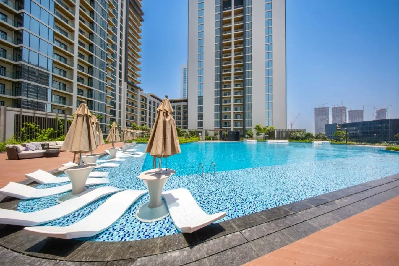 Una piscina en la azotea con tumbonas blancas curvas está rodeada de edificios altos.