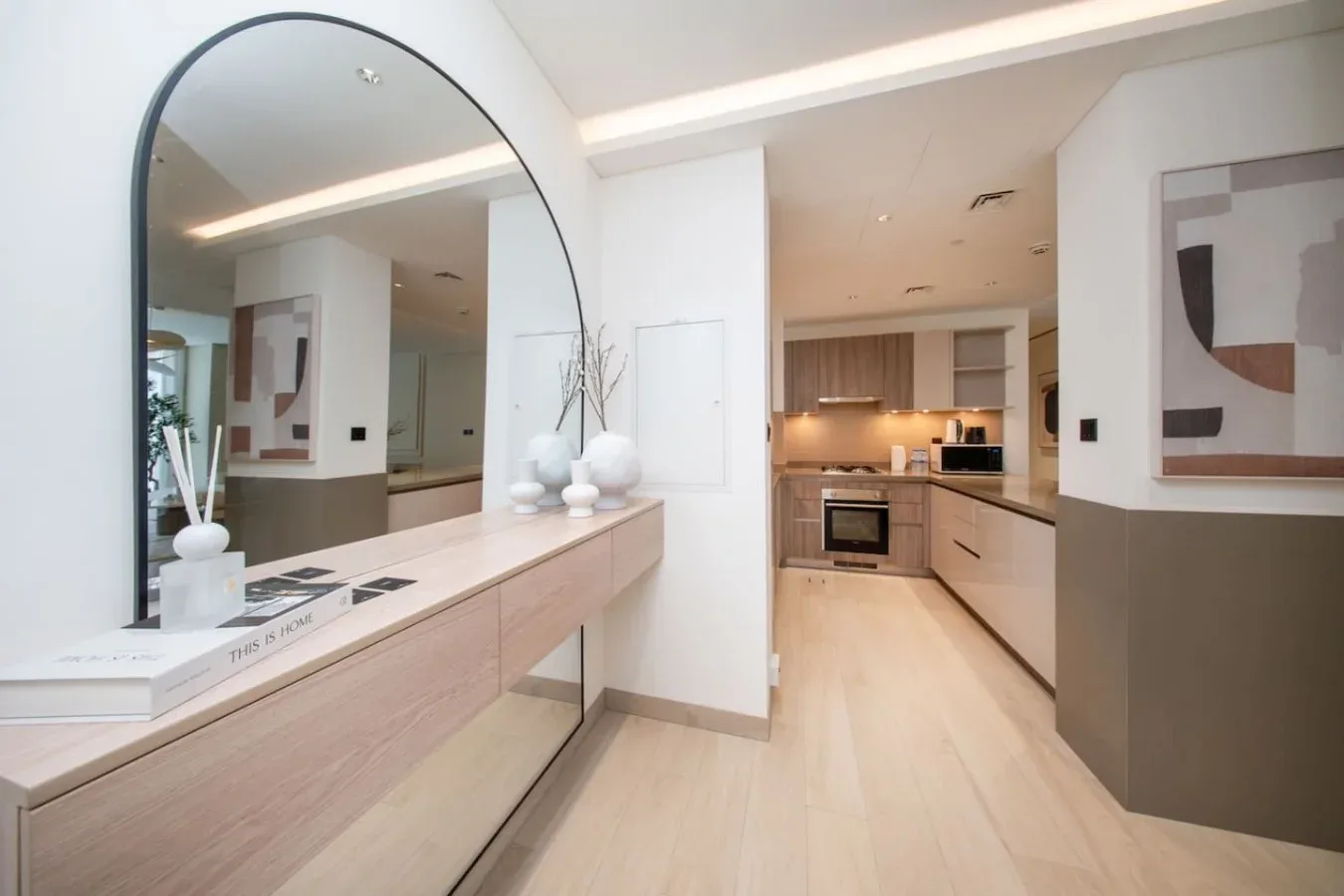 Una cocina moderna y luminosa junto a un pasillo, con gabinetes claros y arte abstracto enmarcado.
