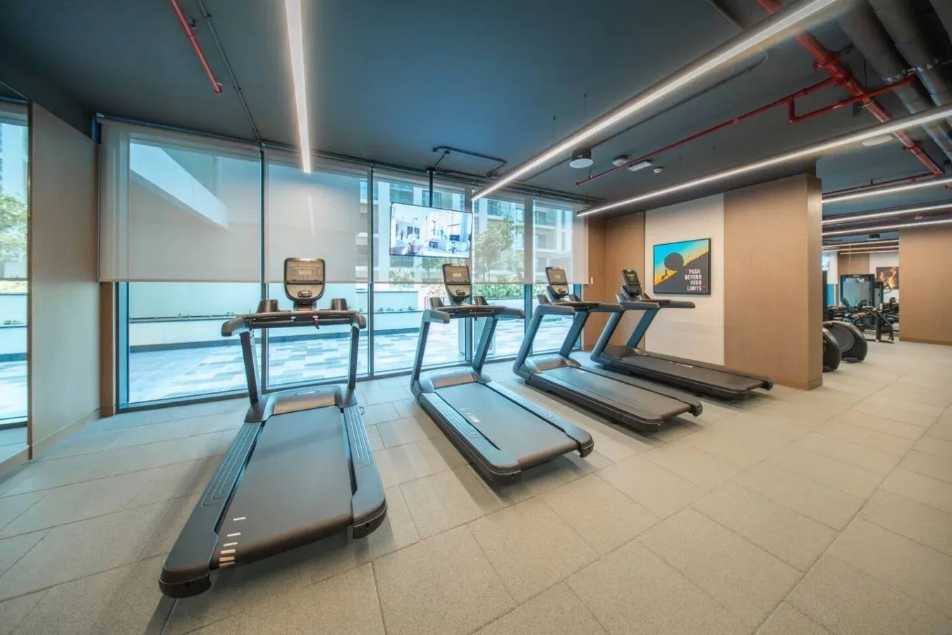 Un gimnasio con cintas de correr junto a grandes ventanales.