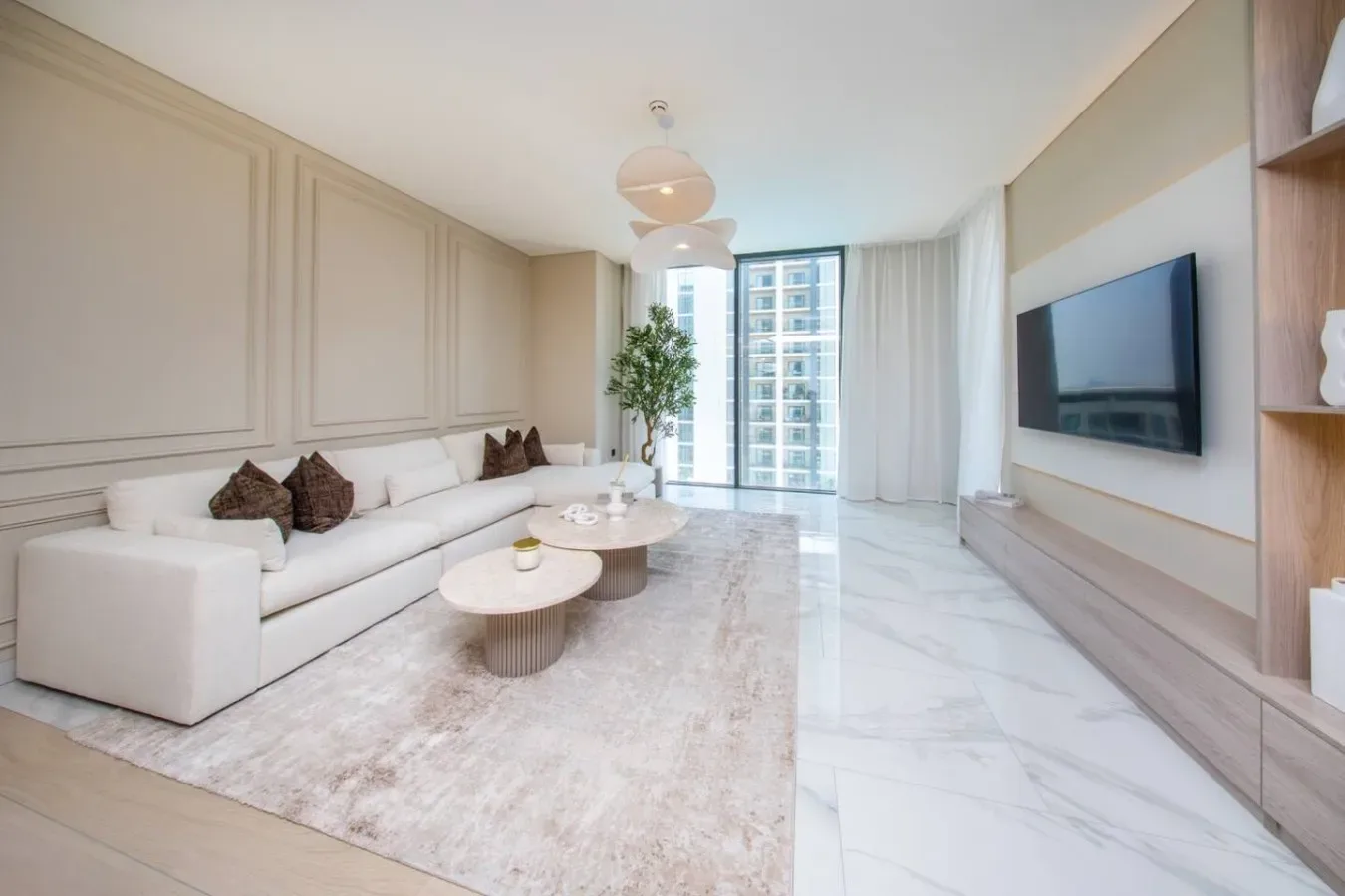 Una sala luminosa con asientos blancos, una alfombra y un televisor en la pared.