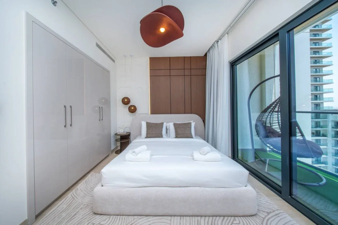 Un dormitorio luminoso con una cama blanca junto a grandes puertas de vidrio.