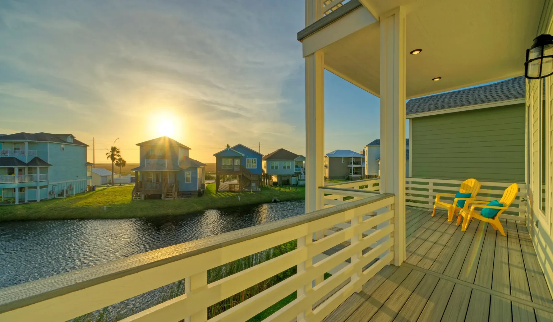 A covered waterfront deck overlooks a canal and nearby houses at sunset.
