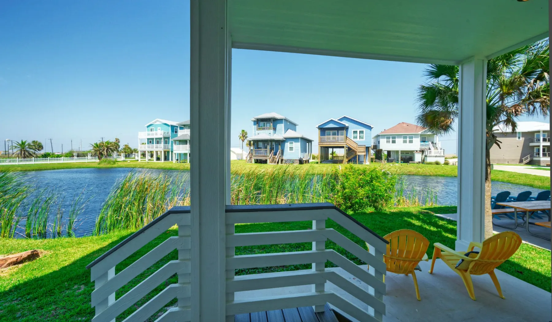 A covered porch overlooks a canal, with outdoor seating and houses across the water.