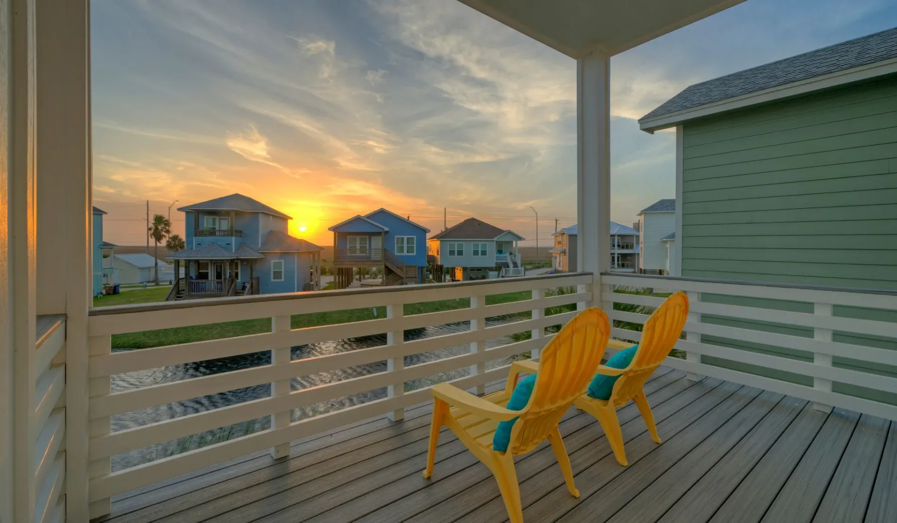 A covered deck overlooks neighboring houses at sunset, with two bright yellow seats.