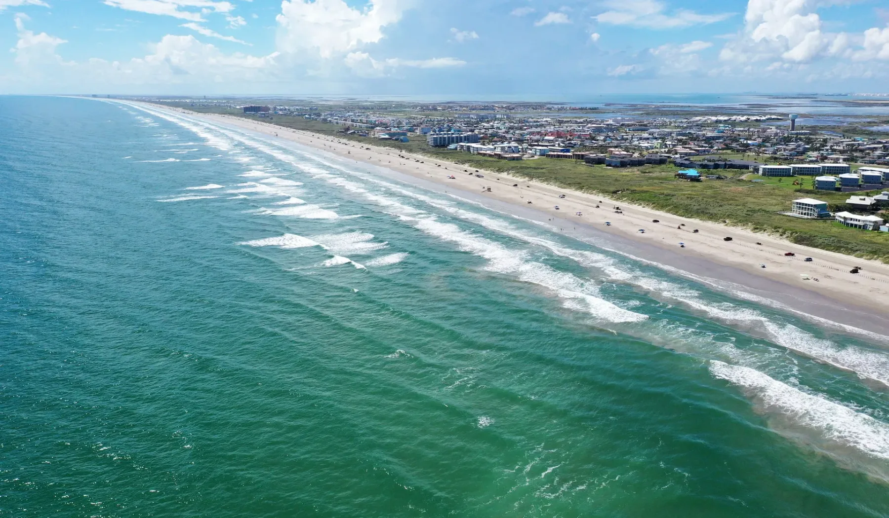 Coastal beach with ocean waves and buildings along the shore.