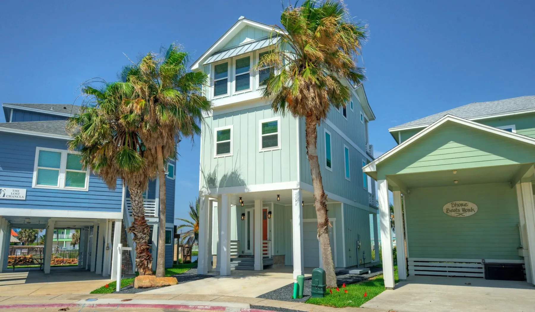A row of colorful coastal houses stands beneath palm trees.
