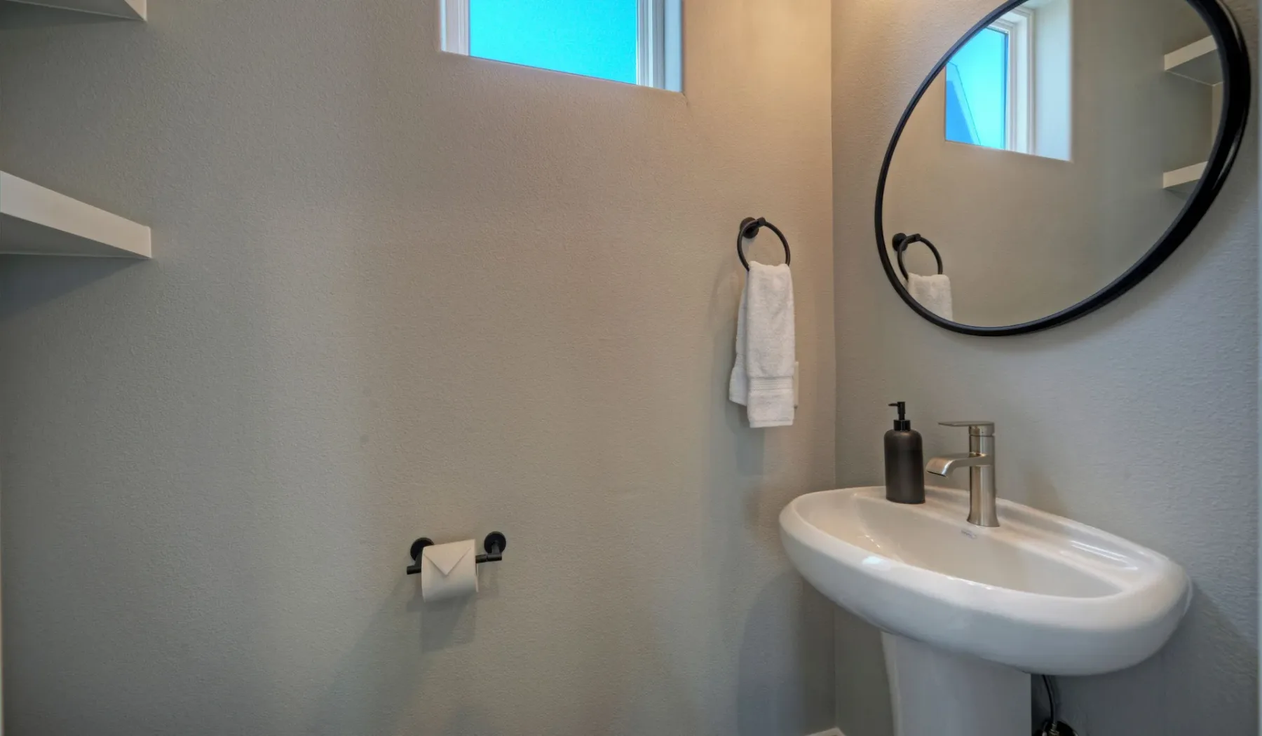 A bathroom with a sink, oval mirror, and towel hanging on the wall.