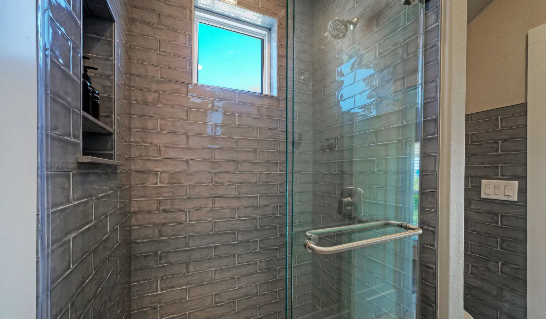A tiled shower with a glass panel and a small window.