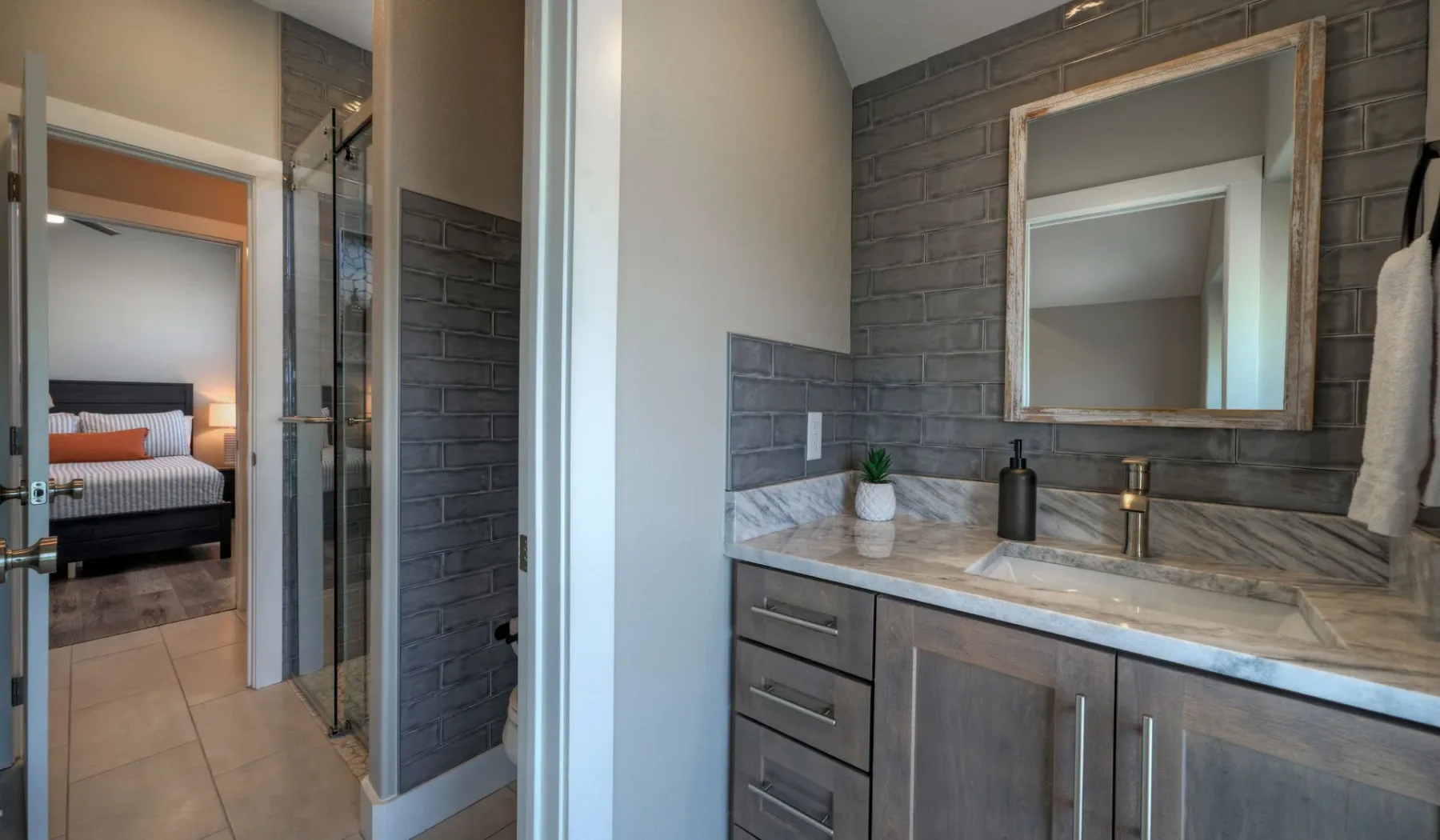 A bathroom vanity with a mirror and sink sits beside a tiled shower.