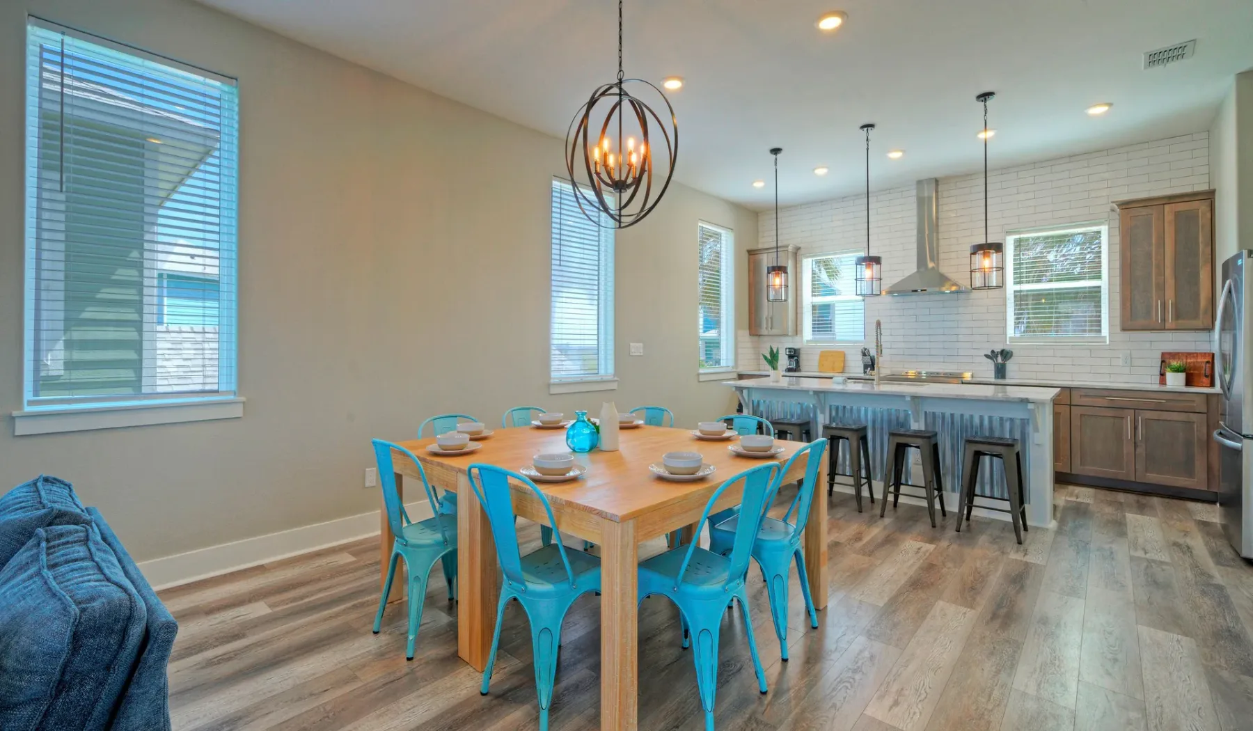 An open dining and kitchen area with a wooden table and turquoise seating.