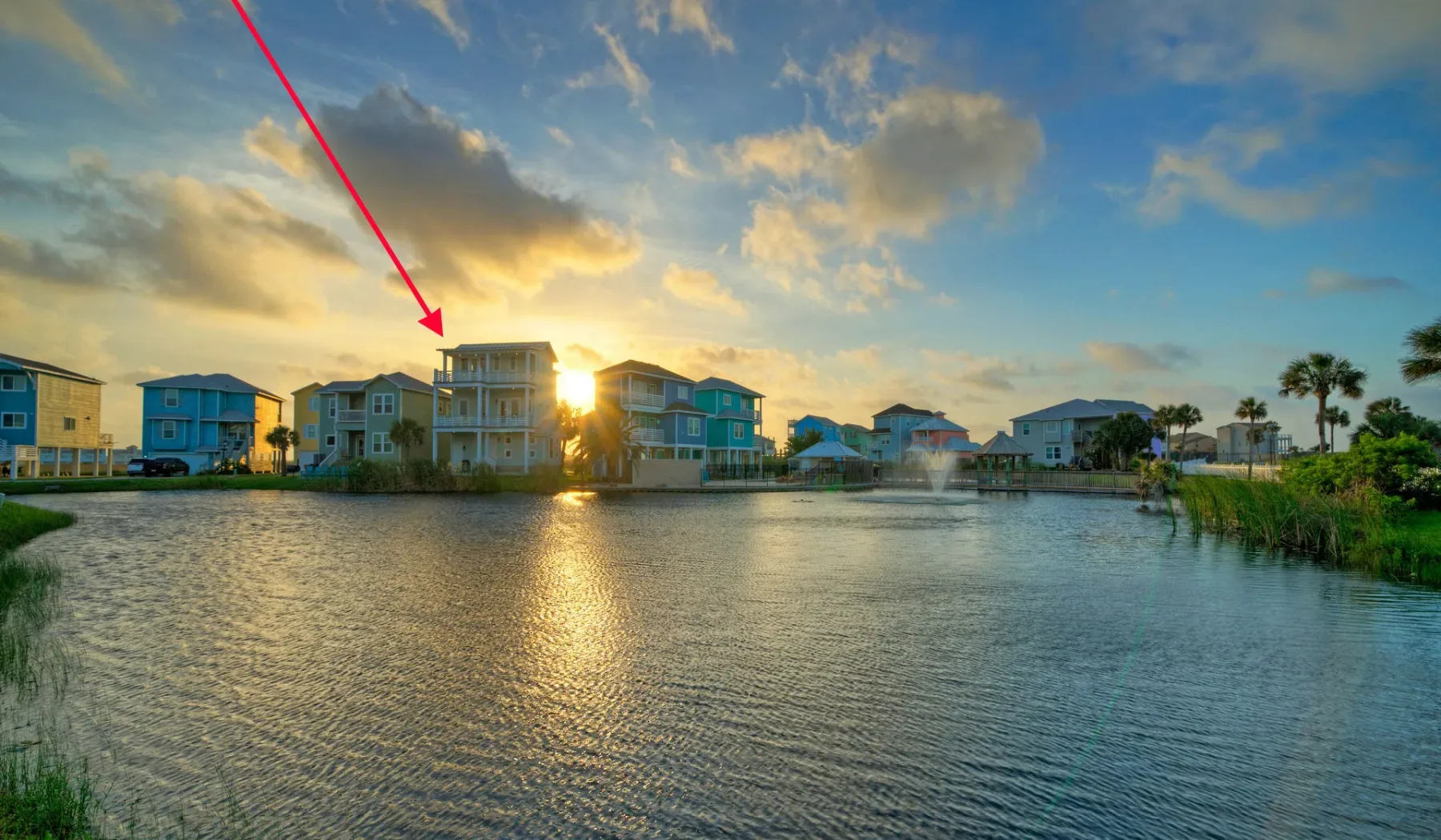 A waterfront neighborhood of houses sits beside calm water at sunset.