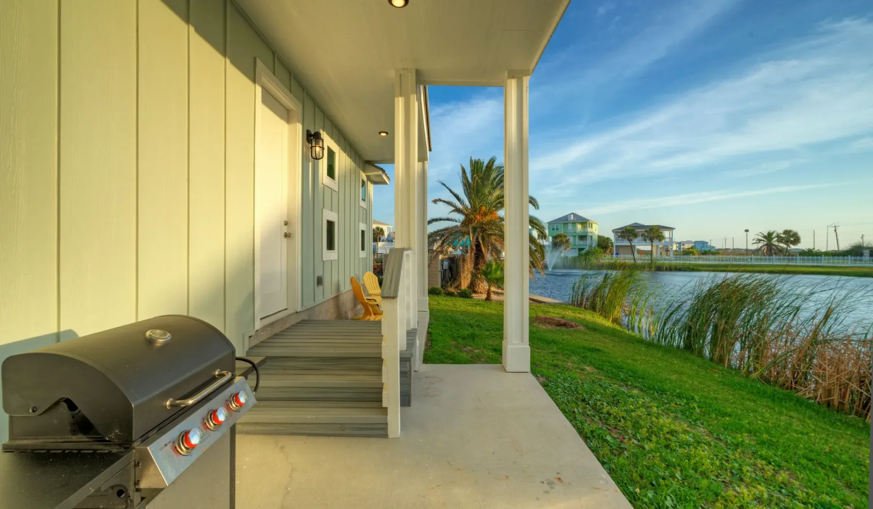 A covered outdoor patio with a grill beside a grassy waterfront.
