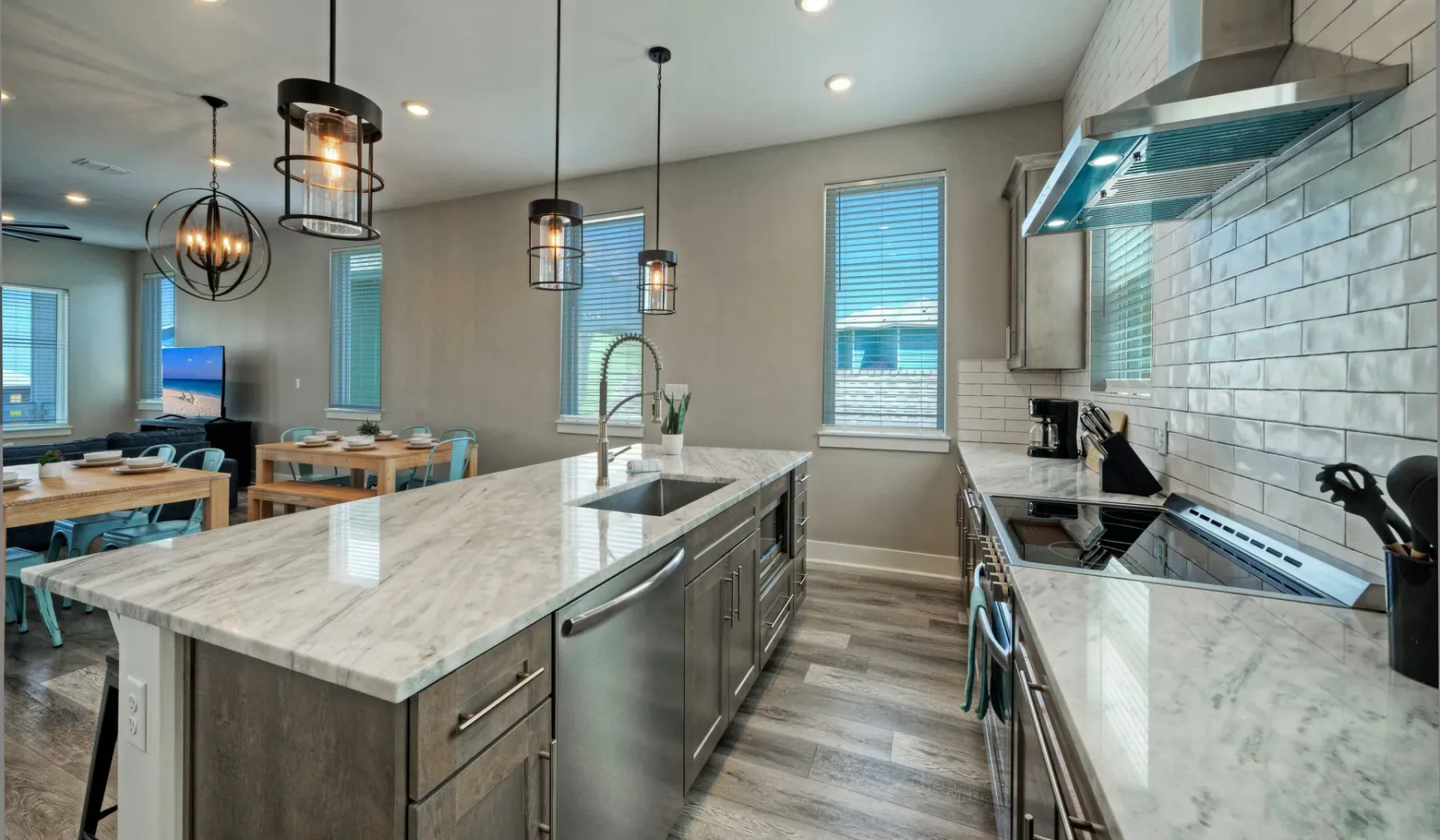 A modern kitchen with a large island, pendant lights, and a dining area.
