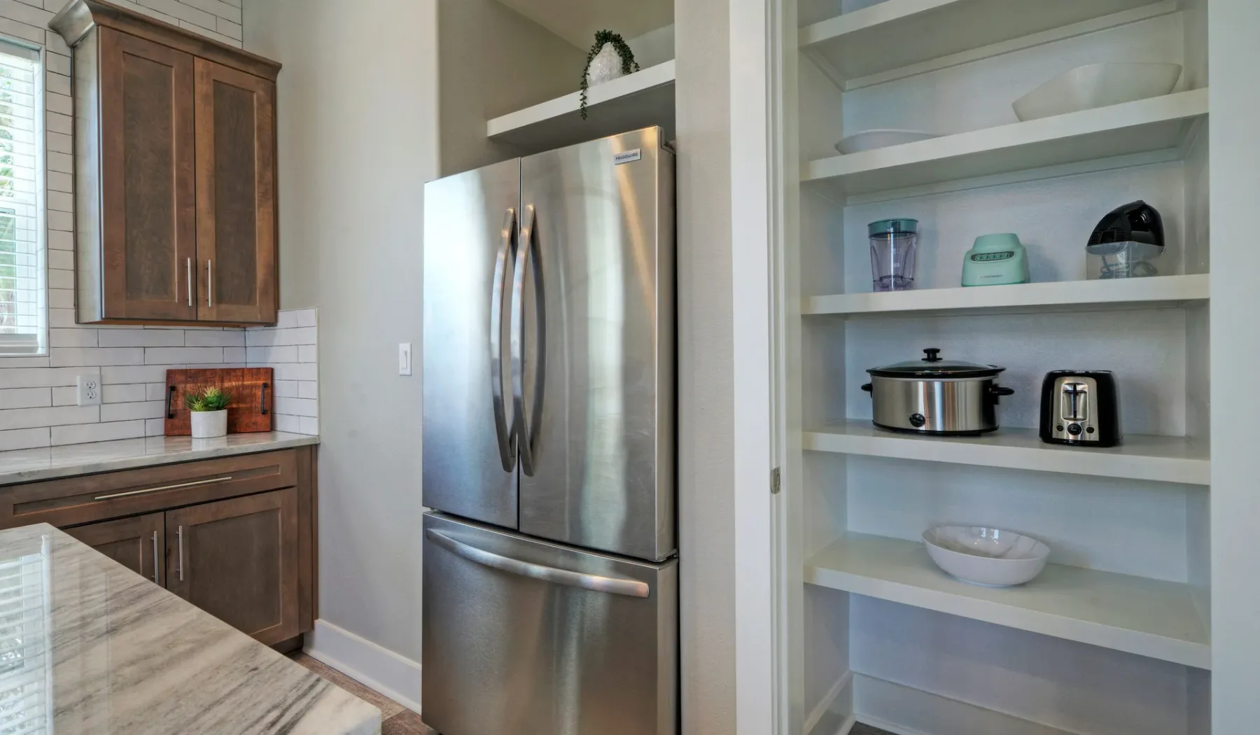 A kitchen with a stainless-steel refrigerator and open shelves holding small appliances.