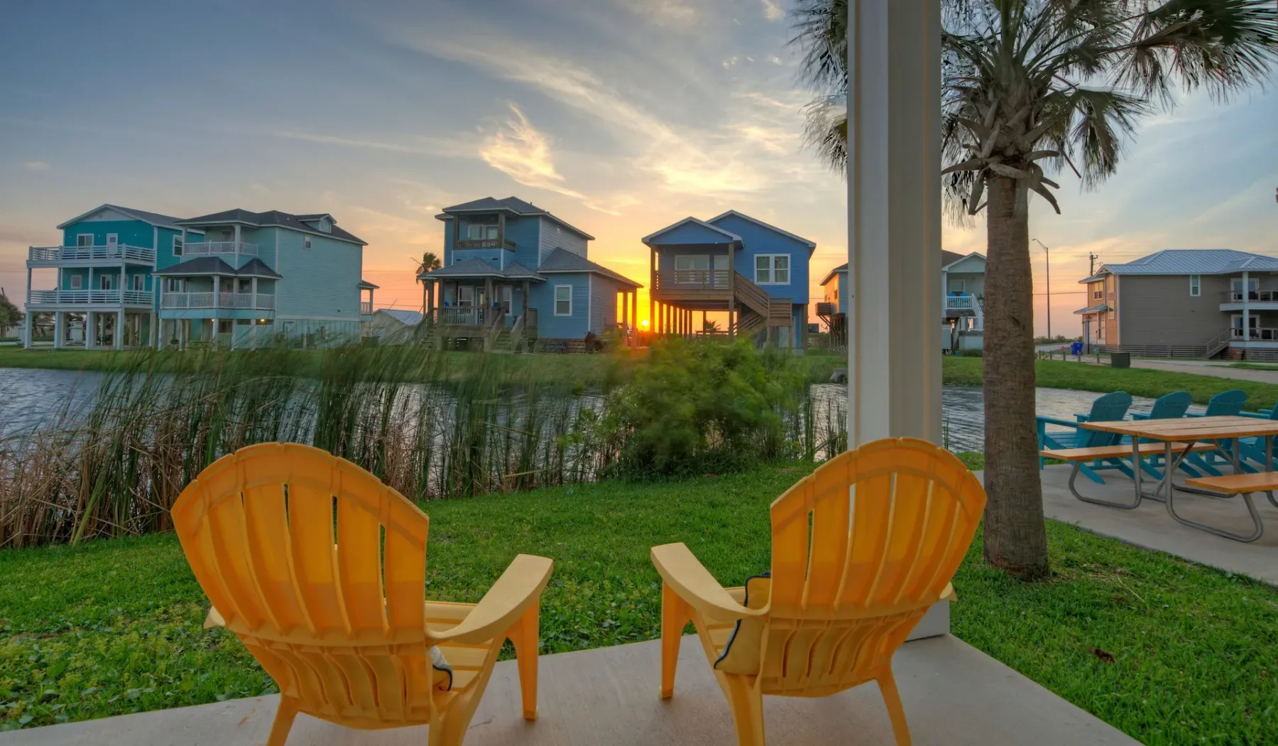 Outdoor seating overlooks a grassy waterfront neighborhood at sunset.