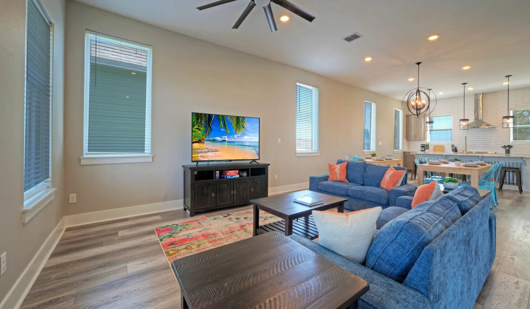 An open-plan living area with blue seating, a television, and a kitchen beyond.