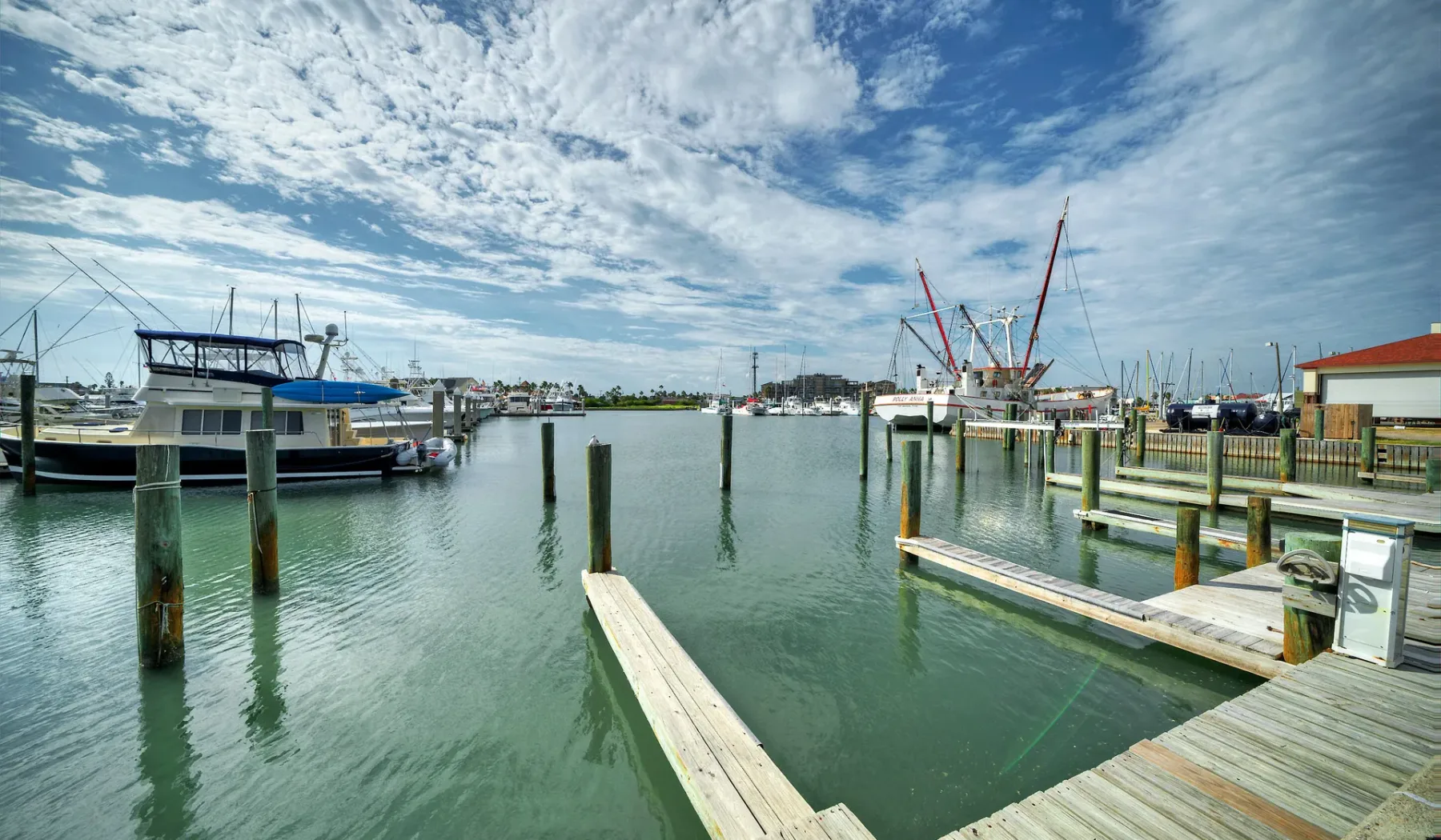 A marina with boats, docks, and cranes beneath a partly cloudy sky.