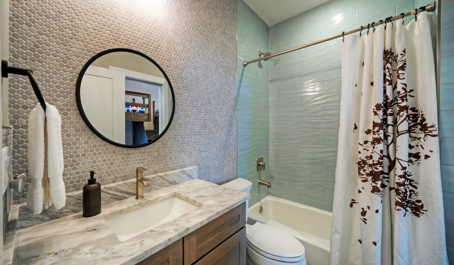 A bathroom vanity with a round mirror beside a bathtub and shower curtain.