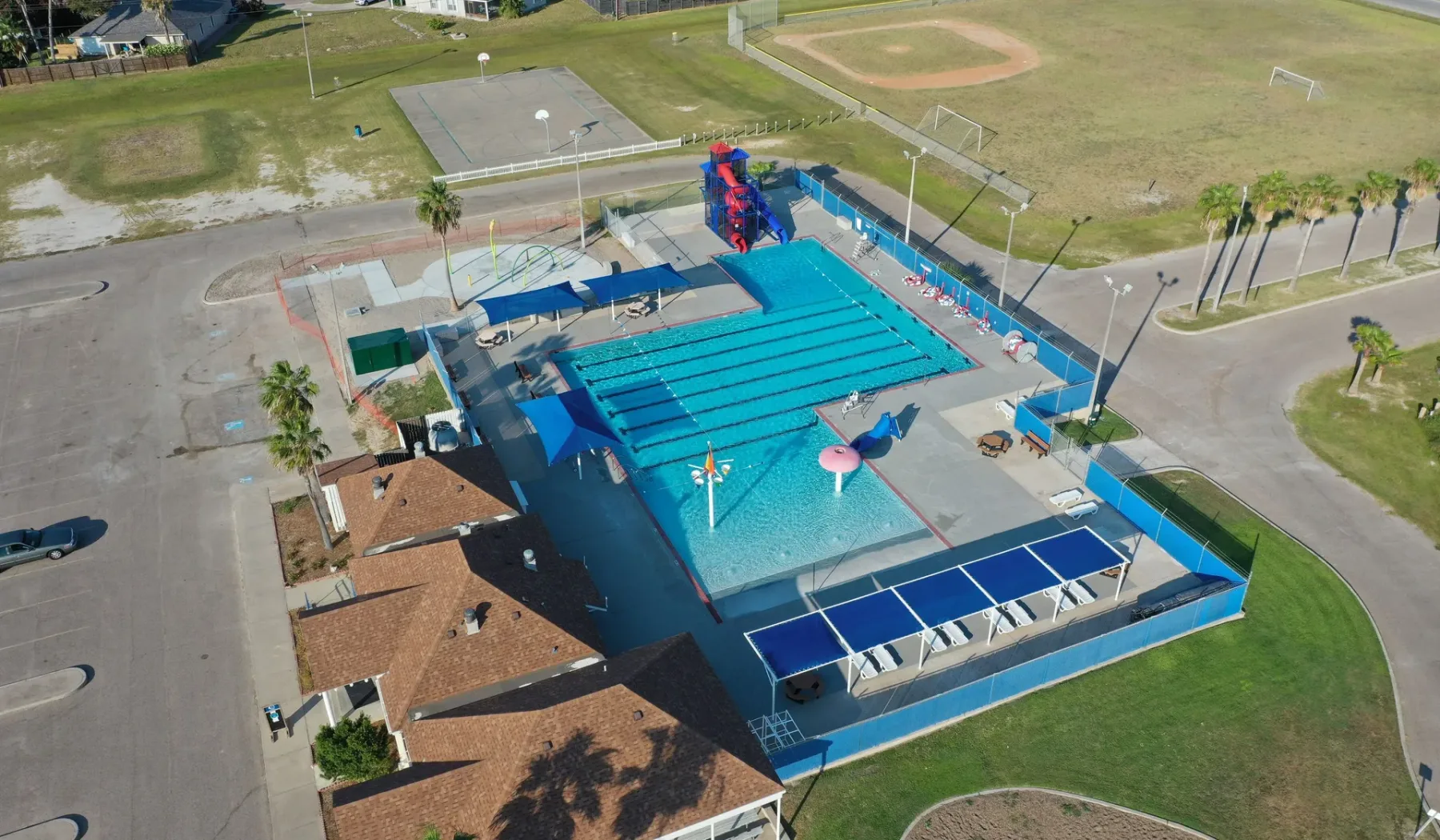An outdoor swimming pool with blue water slides sits beside open sports fields.